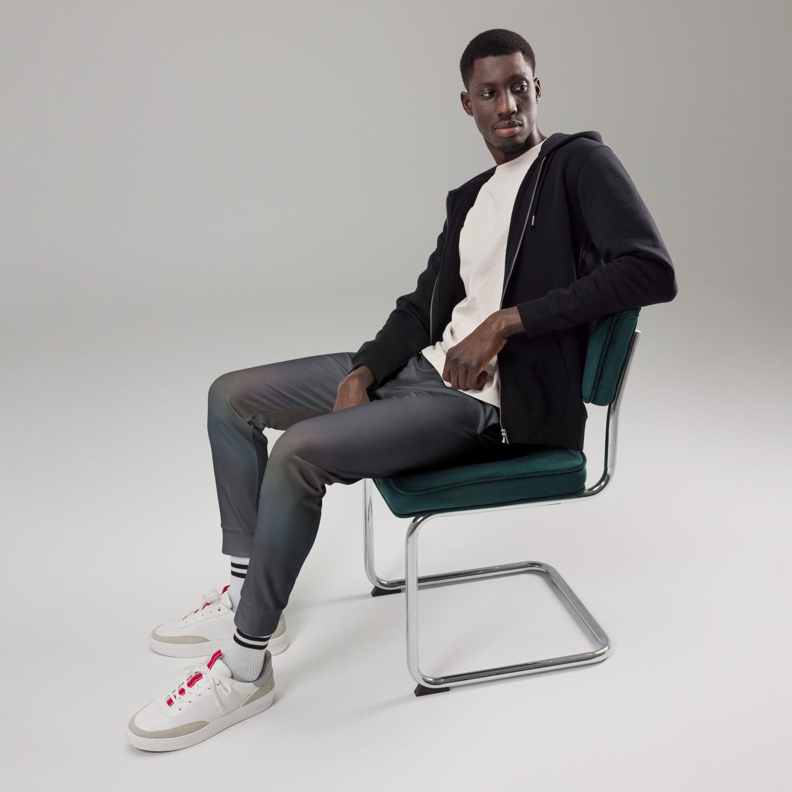 Seated model wearing Quiet Spectrum joggers with the dark translucent colour field visible across the legs