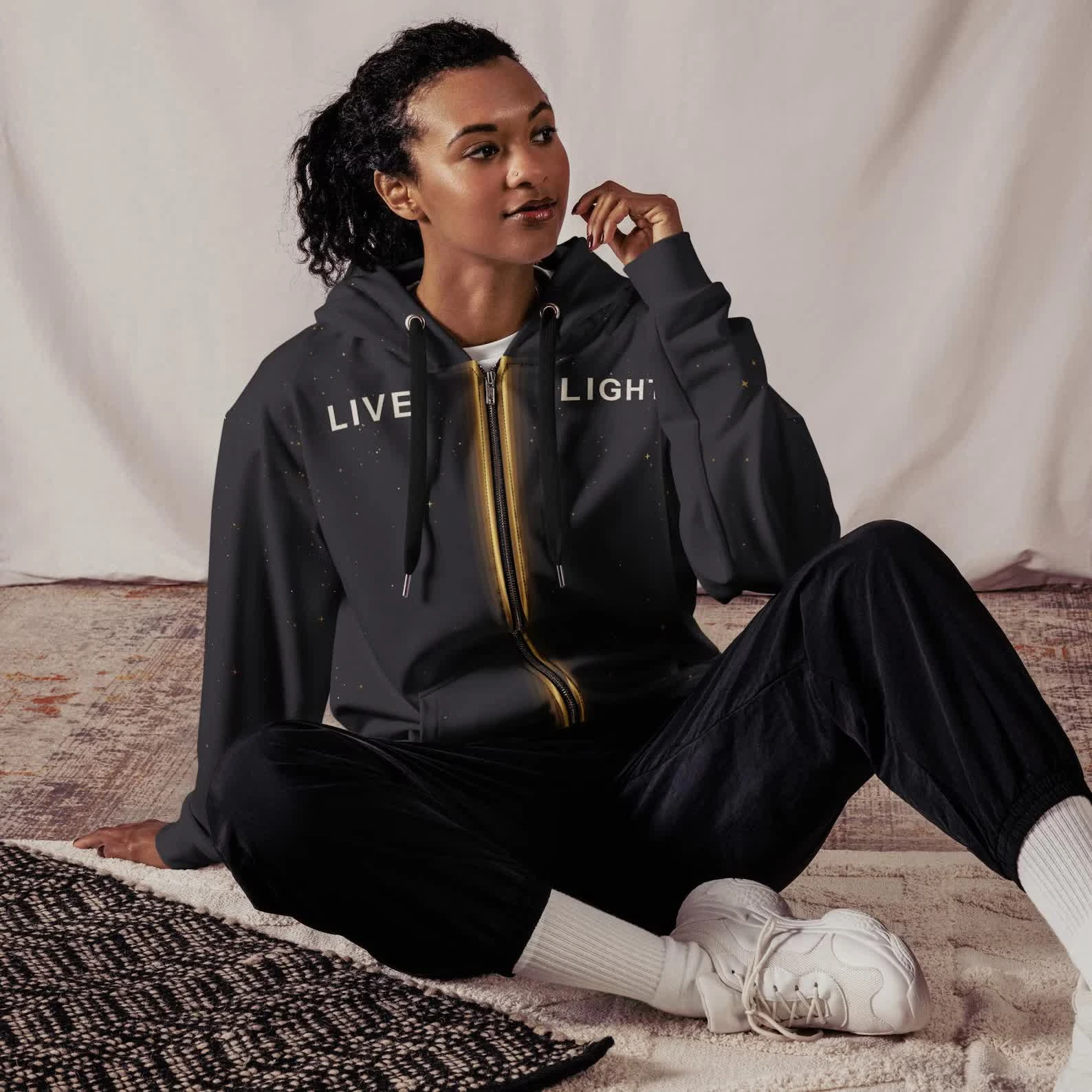 Model seated in the dark Live Light zip hoodie with the glowing zipper design and LIVE LIGHT text across the chest