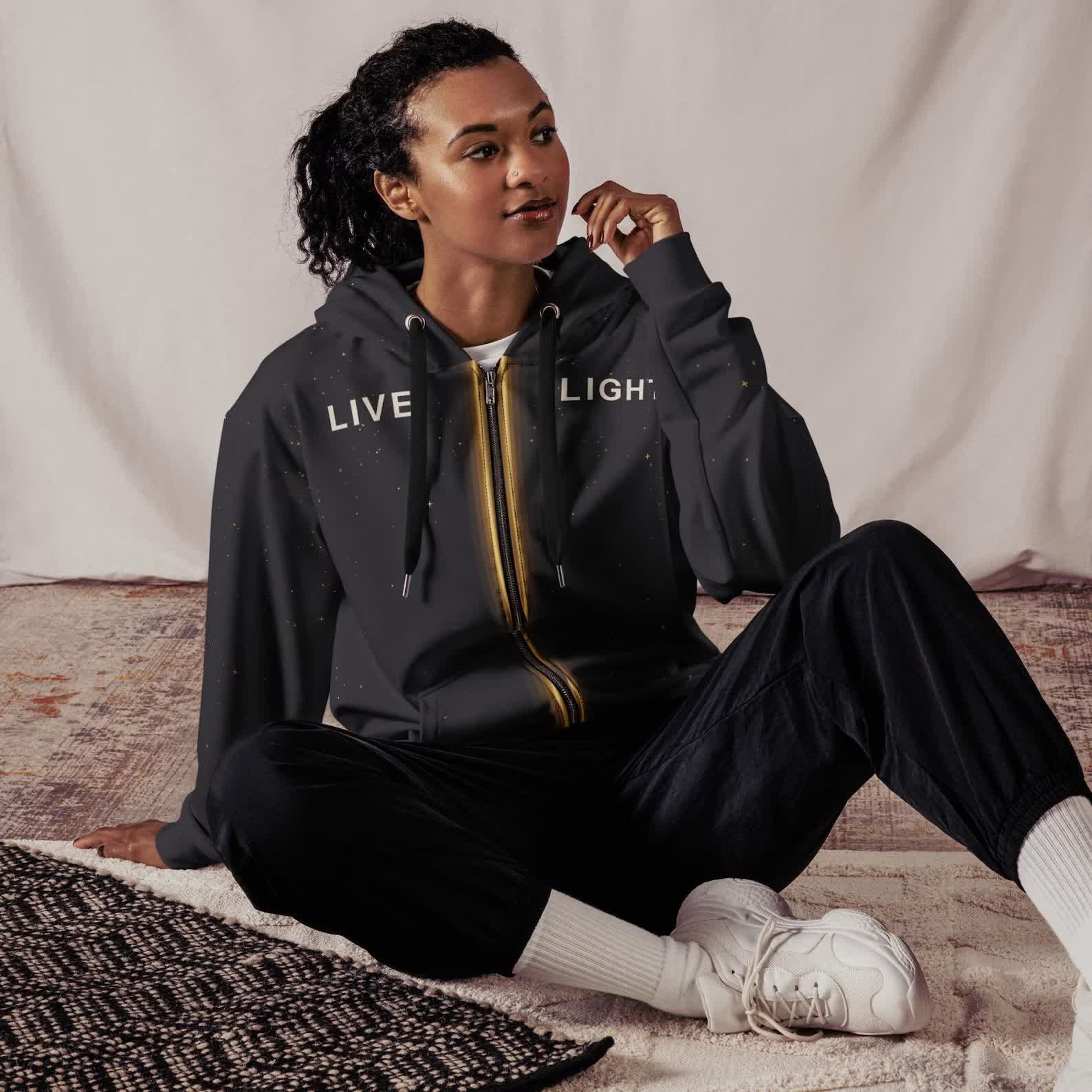 Model seated in the dark Live Light zip hoodie with the glowing zipper design and LIVE LIGHT text across the chest